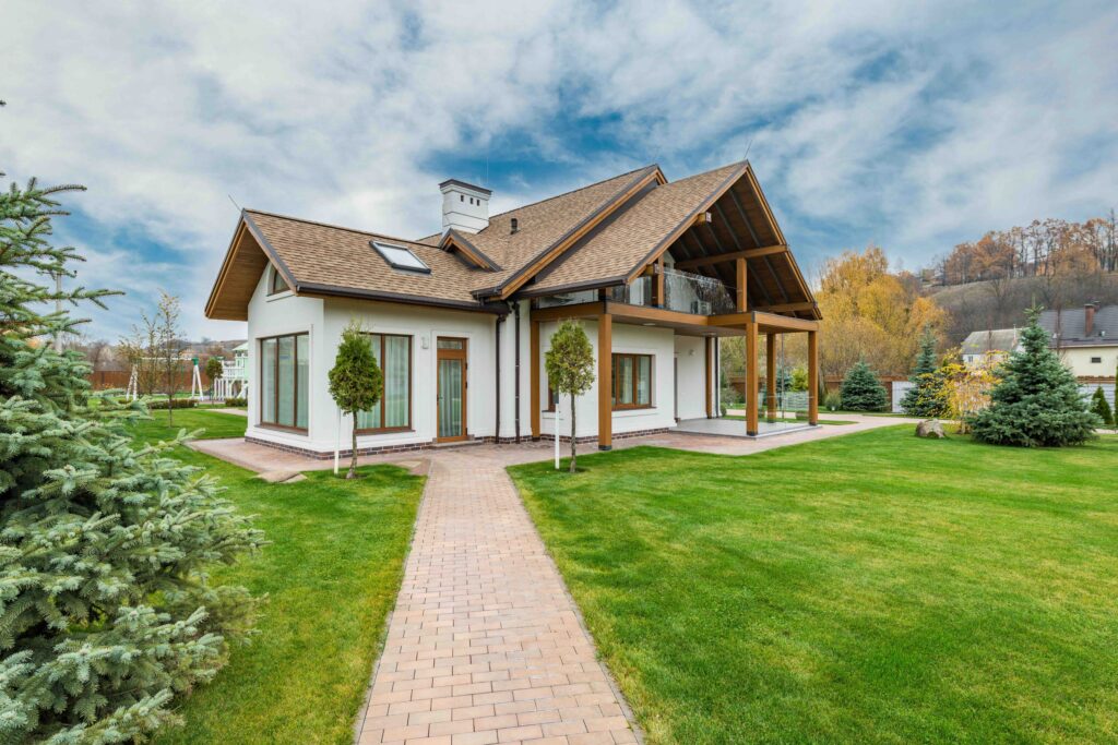 Modern L-shaped house with brown roof, white walls, green lawn, and brick walkway to entrance.