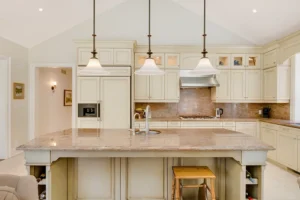 Elegant cream kitchen with marble countertops, pendant lights, and built-in appliances.