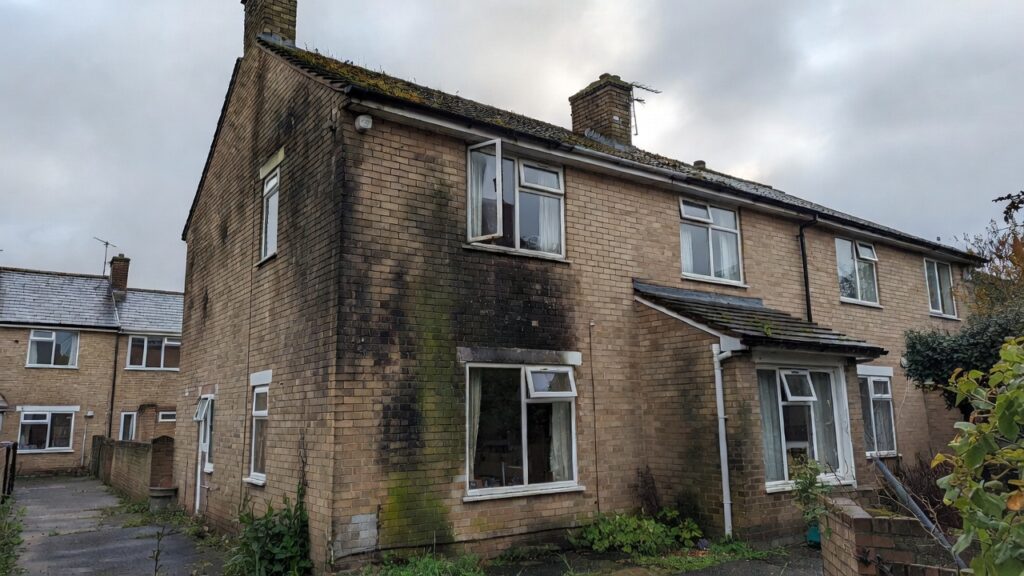 Exterior of a UK brick house with extensive black mould and damp stains on the walls under overcast sky
